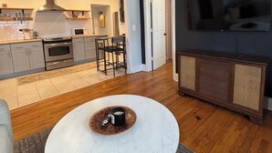A modern kitchen with a central island, a dining area with a round table, and a living area with a TV. - Cozy East Nashville Home w Fenced-In Backyard (Nashville)