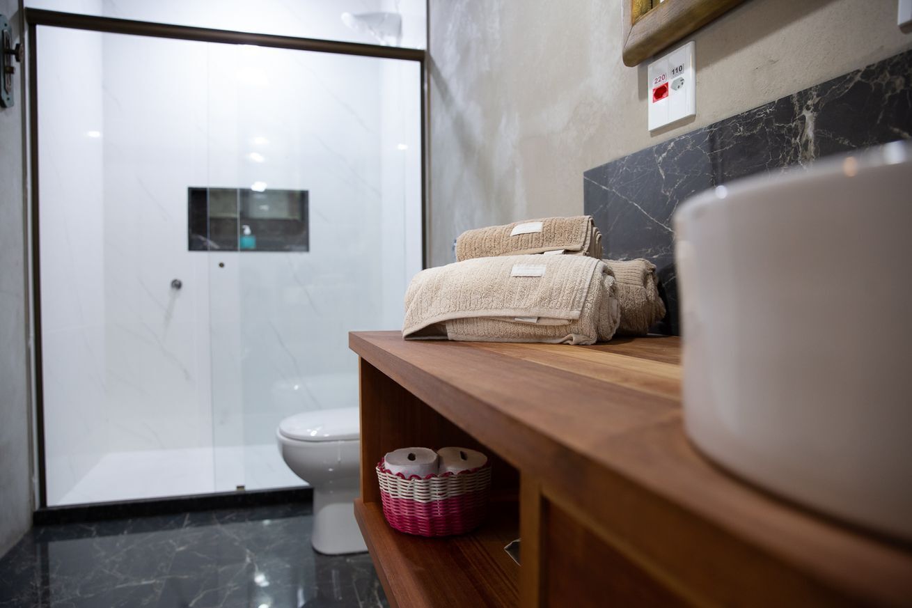 A modern bathroom with a glass shower enclosure, a white toilet, and a wooden vanity with towels and a basket.