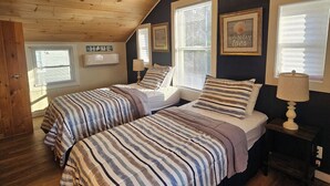 Een slaapkamer met twee bedden, houten plafond en een donkere muur met ingelijste foto's.
