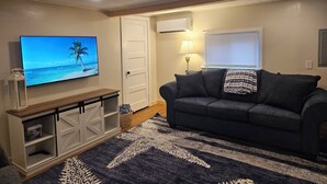 Een woonkamer met een televisie aan de muur, een bank, een houten kast en een kamerkleed met een patroon.