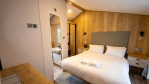 A hotel room with a large bed, a wooden headboard, a bedside table with a lamp, and a small bedside table with a vase.