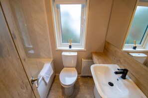 Une petite salle de bain comprenant des toilettes, un bidet et un lavabo, avec une fenêtre et un lambris en bois.