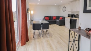 A modern living space with a dining area, sofa, kitchen, and large windows.