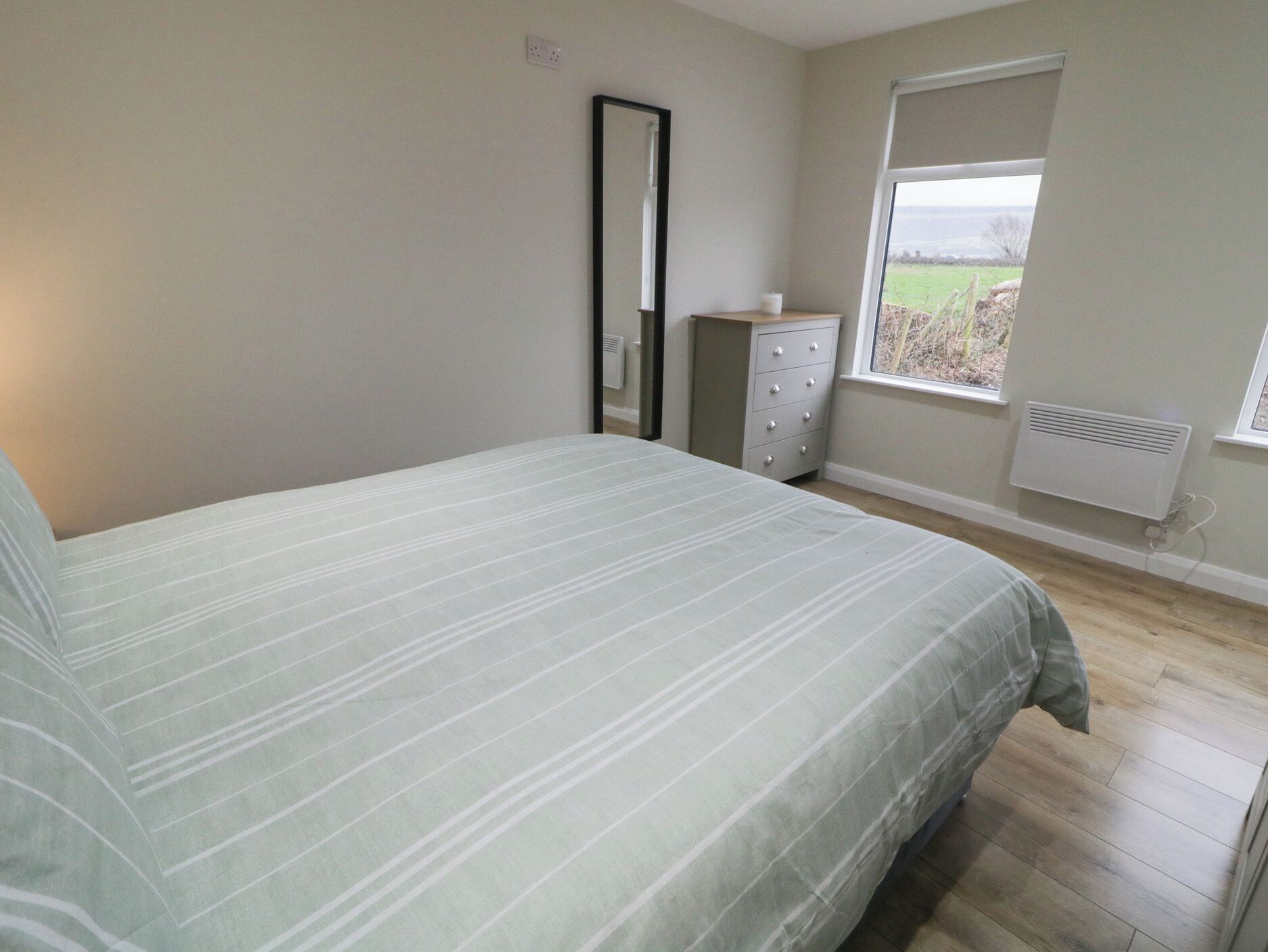 A bedroom with a bed, a dresser, a mirror, and a window with a view of the outdoors.