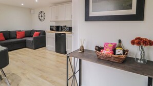 A modern living room with a grey sofa, a dining table, and a kitchen area with white cabinets and a dishwasher.