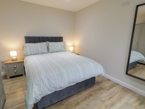 A bedroom with a bed, bedside tables, a mirror, and a wardrobe. - Binevenagh Point Cabin (Limavady)