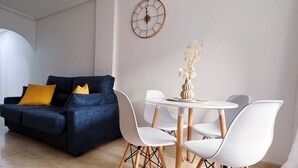 Una sala moderna con un sofá azul oscuro, sillas blancas y una mesa redonda.