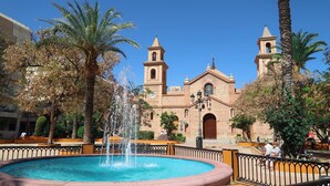 Un edificio histórico con dos torres, una fuente y palmeras en un patio.