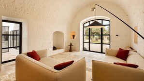 Une pièce spacieuse avec un haut plafond en arc de cercle, une grande fenêtre et une vue sur l’extérieur. On y trouve deux canapés avec des coussins rouges et une petite table avec une lampe.