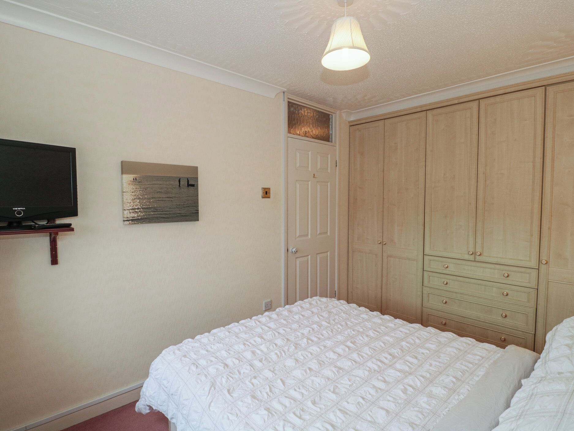Een slaapkamer met een bed, een televisie, een kledingkast en een schilderij aan de muur.