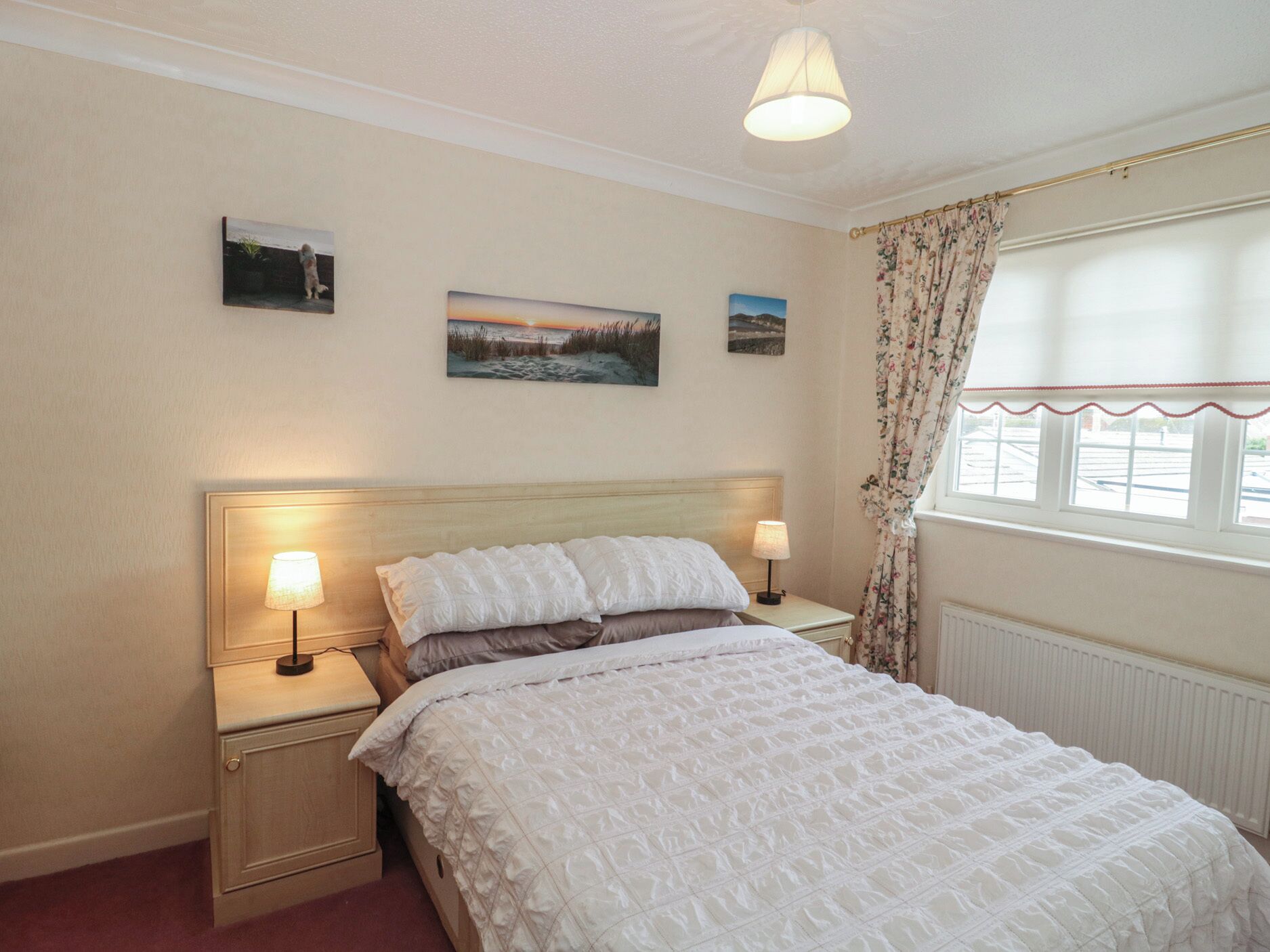 A bedroom with a large bed, two bedside tables with lamps, a headboard, and three framed pictures on the wall.
