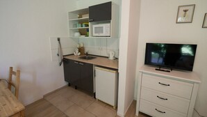 Ett kompakt kök med mikrovågsugn, diskho och ett litet kylskåp. Här finns ett matbord i trä och en platt-TV som är monterad på ett skåp.