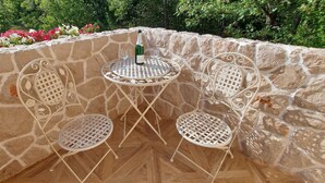 A stone wall with a small table and two chairs, a bottle of wine, and a glass on the table.