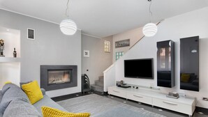 A modern living room with a fireplace, sofa, TV, and staircase.