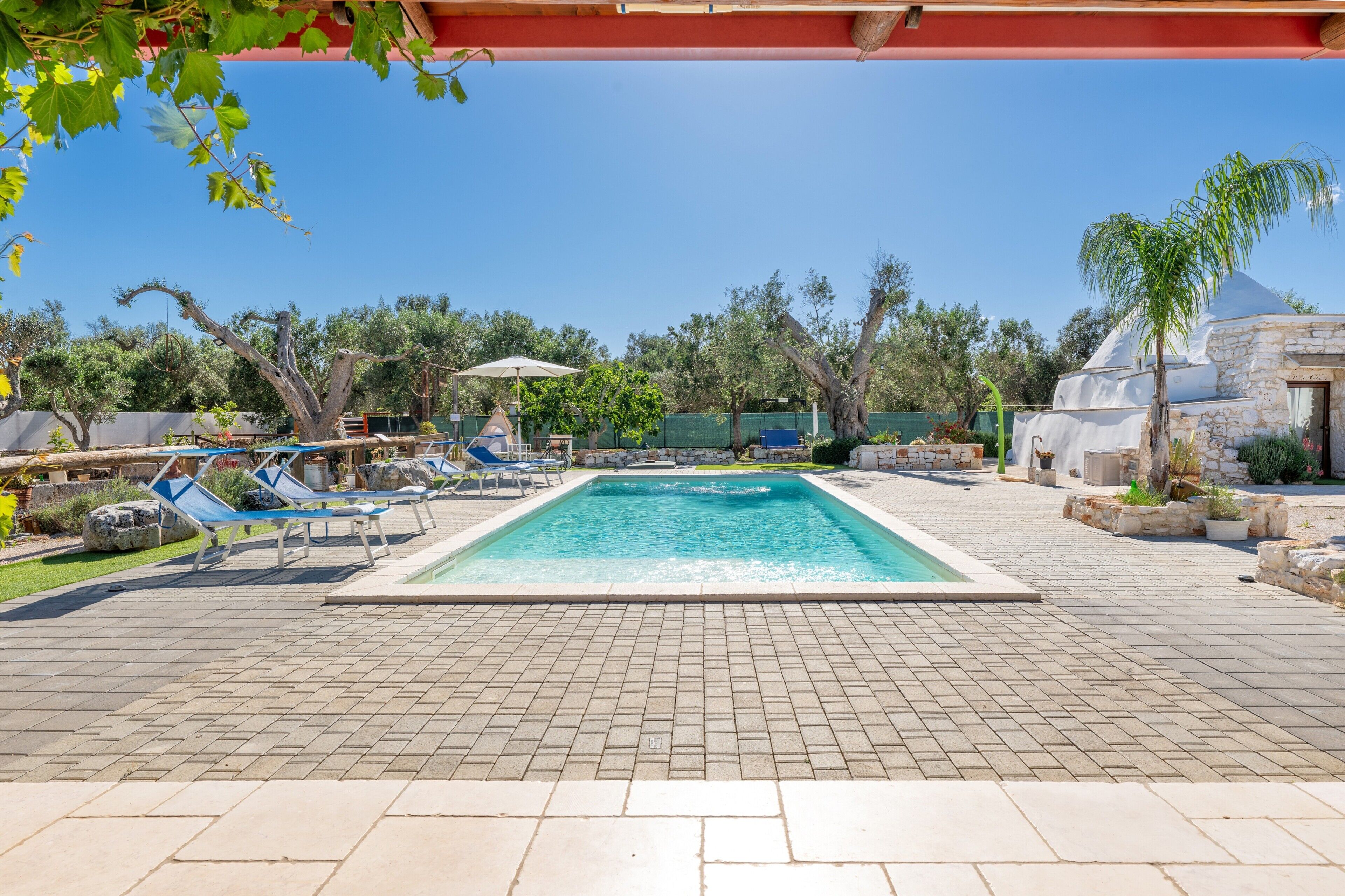 A swimming pool with lounge chairs, a pergola, and a stone building in the background.