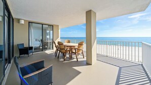 A balcony with a table and chairs, a view of the ocean, and a glass door leading to a room. - 🐠🌞Beachfront w/ Corner Balcony | Indoor + Outdoor Pools | Romar Place 506🌞🐠 (Orange Beach)