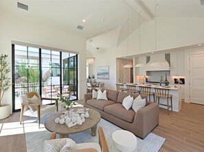 Amplia sala de estar con un sofá grande, una mesa de comedor y sillas. Hay una cocina equipada con electrodomésticos modernos y un ventanal con vistas a un balcón.