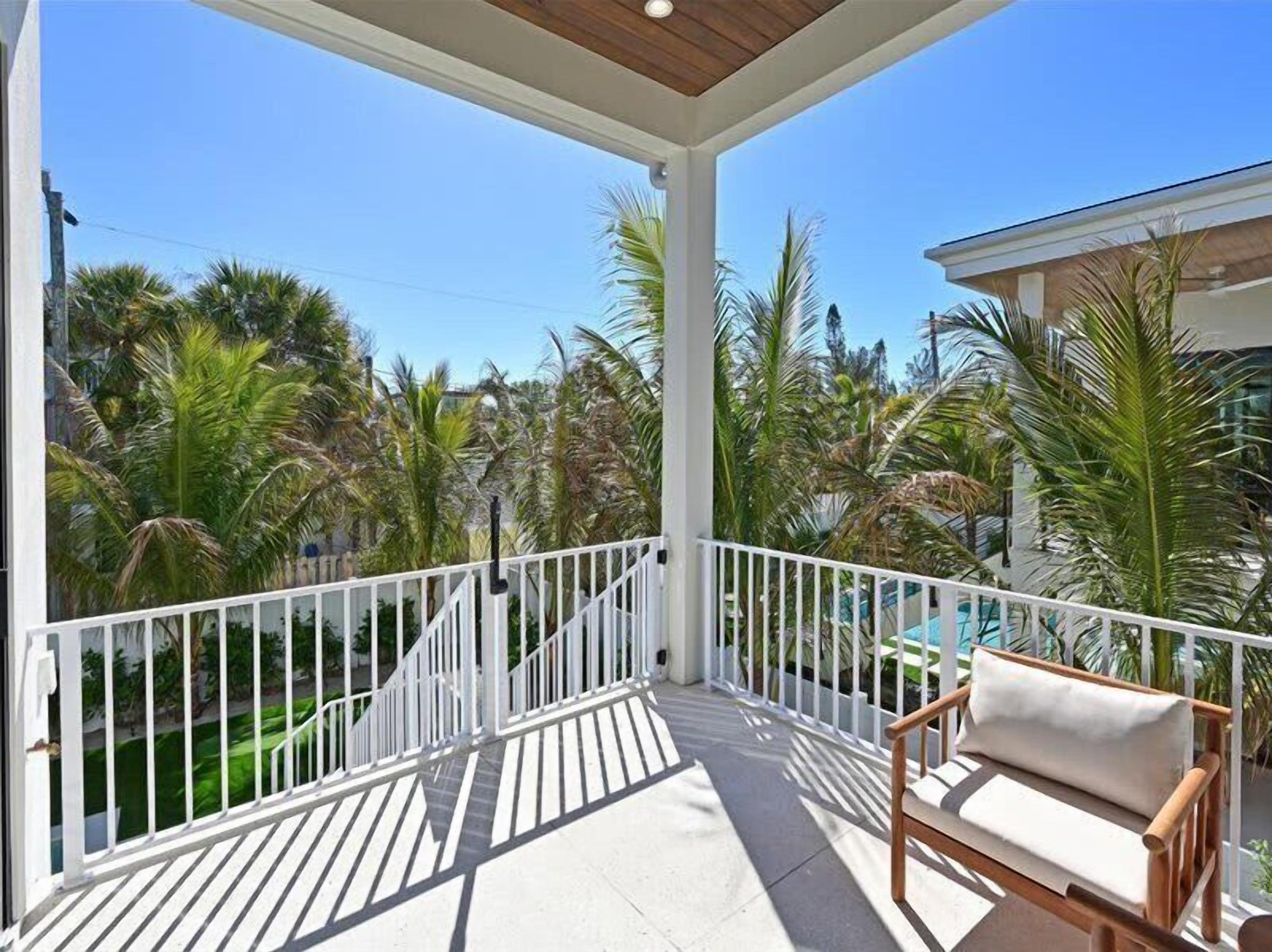 Un balcon abrité avec des balustrades blanches, un banc en bois et une vue sur des palmiers et une piscine.