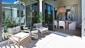 A modern outdoor patio with glass doors leading to a dining area, featuring contemporary furniture and a hanging light fixture. - Palmetto Sunset -Heat Pool/Spa, Steps to Beach! (Anna Maria)