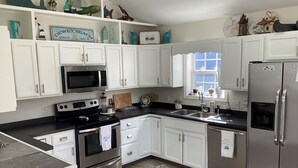 A modern kitchen with white cabinets, stainless steel appliances, and decorative items on shelves. - Fun 3BR House in Rehoboth/Dewey Beach area (Rehoboth Beach)