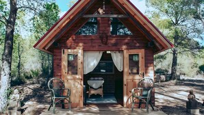 A wooden cabin with a porch, two chairs, and a bed inside.