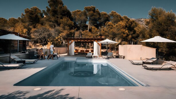 A swimming pool with lounge chairs and umbrellas, surrounded by trees and a pergola.