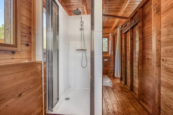 A wooden interior with a glass-enclosed shower, wooden walls, and a window.
