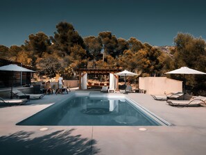 A swimming pool with lounge chairs and umbrellas, surrounded by trees and a pergola.