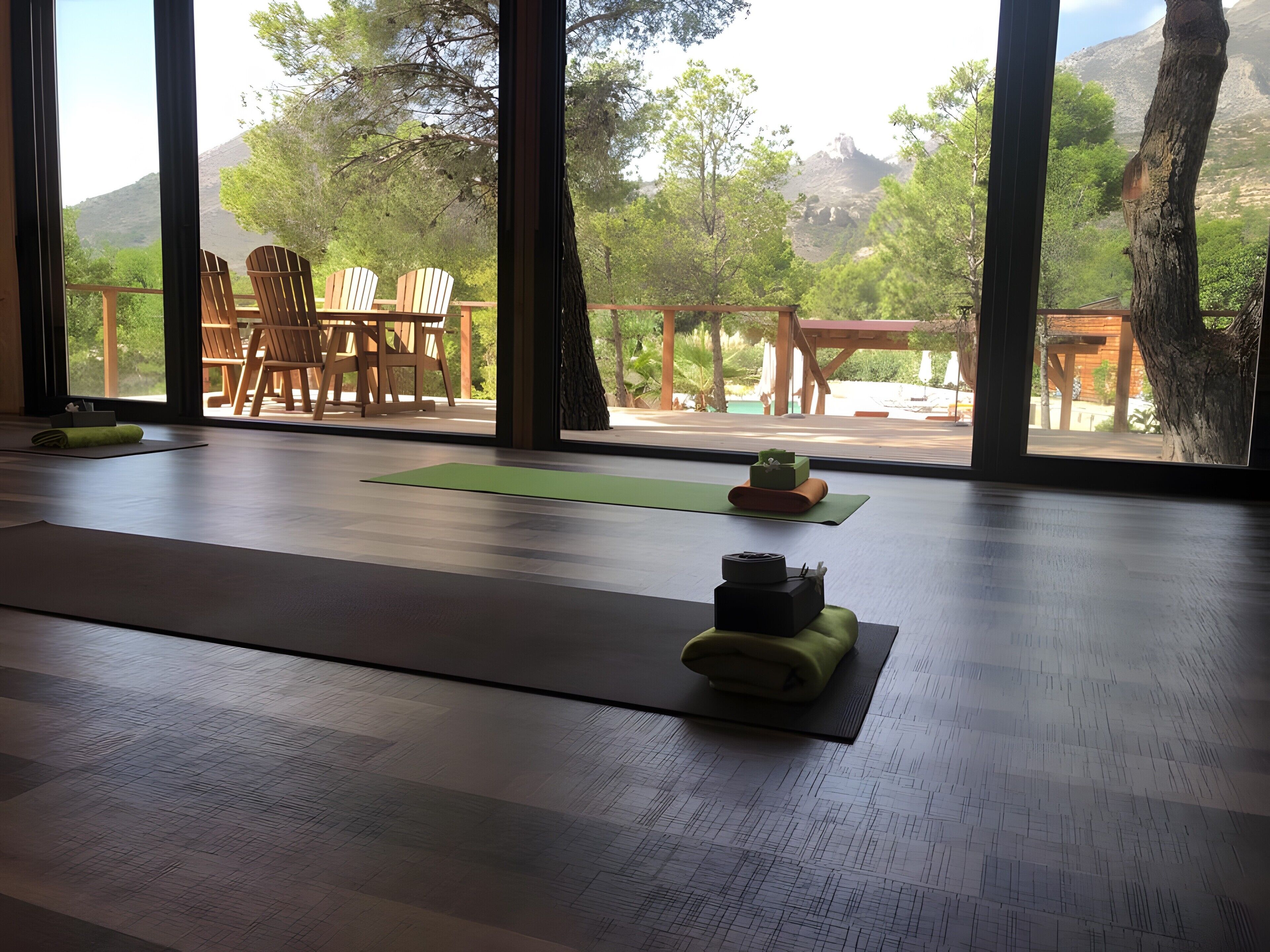 Une pièce dotée de grandes fenêtres, d’un tapis de yoga et d’une table en bois avec des chaises.