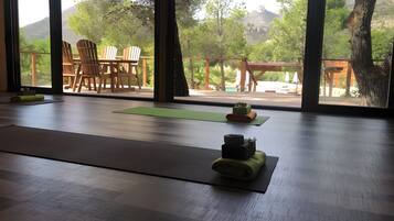Une pièce dotée de grandes fenêtres, d’un tapis de yoga et d’une table en bois avec des chaises.