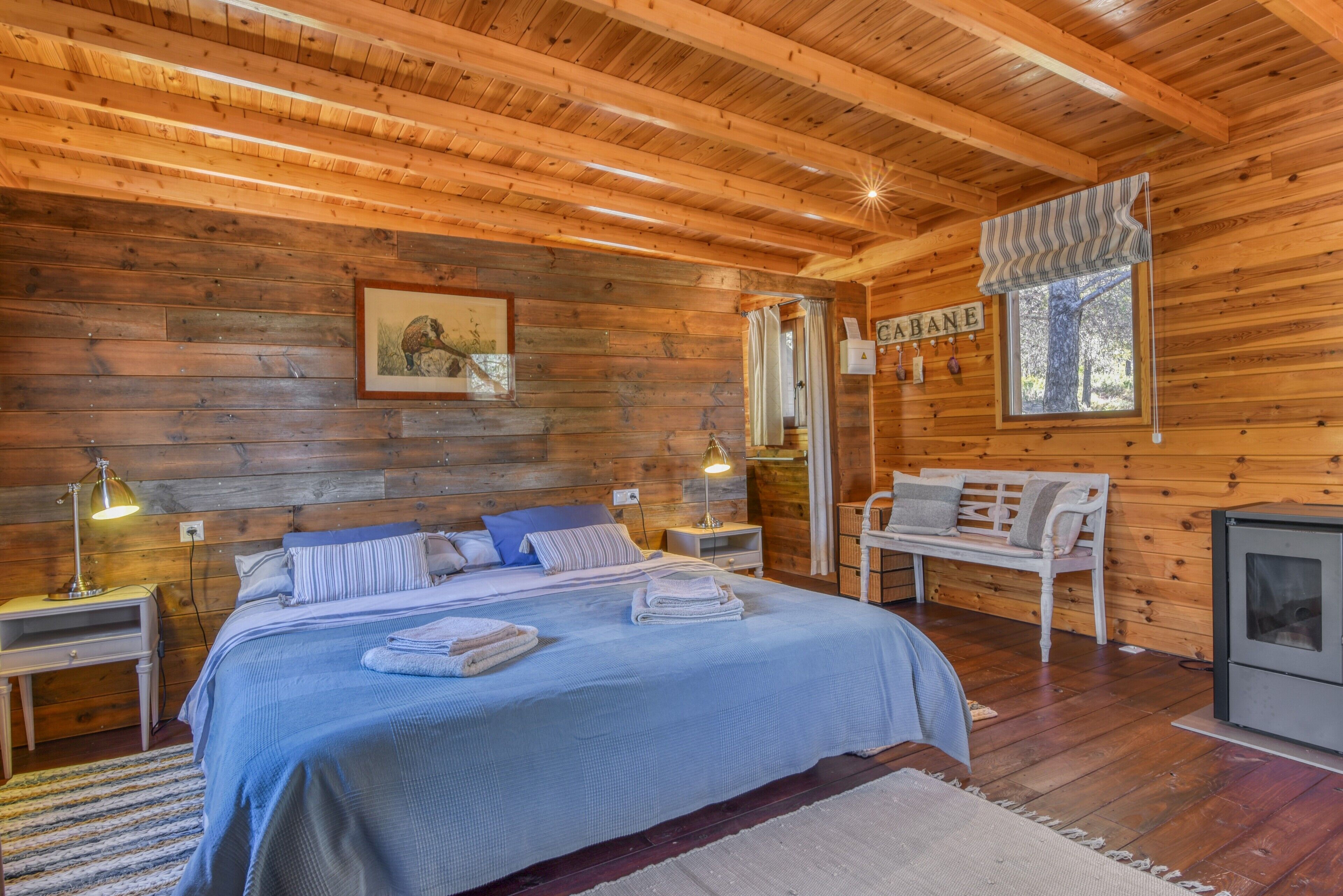 Een houten chalet van binnen met een bed, nachtkastjes, een bankje en een open haard.