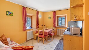 Quarto compacto com cama, mesa de jantar com cadeiras, cozinha compacta e janela com cortinas.