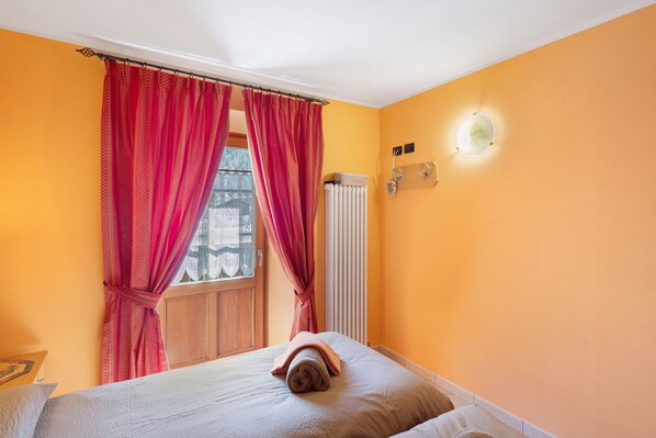 Une pièce comprenant un lit, une fenêtre avec des rideaux, un radiateur et un luminaire fixé au mur.