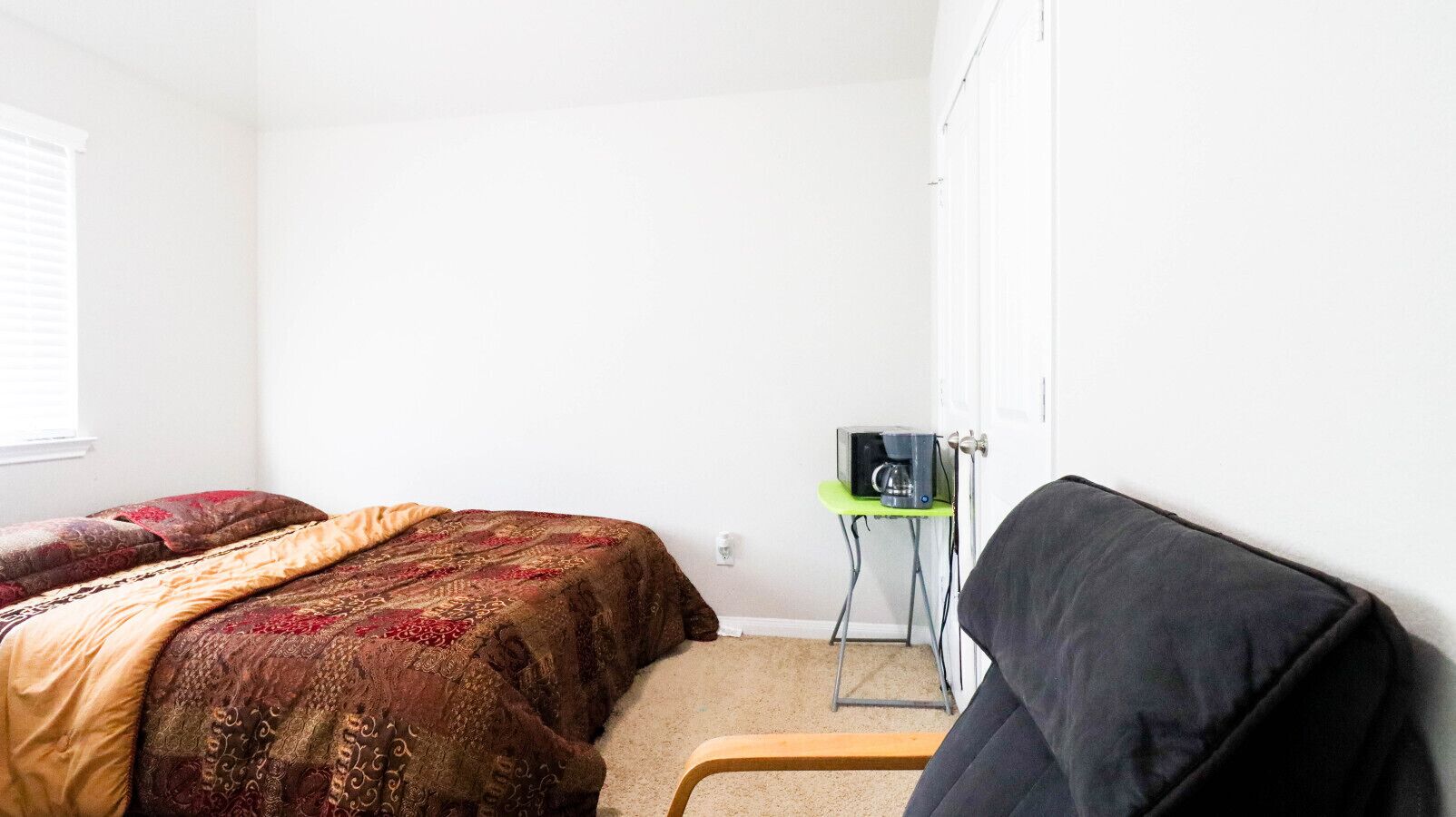 Een slaapkamer met een bed, een stoel en een klein tafeltje met een koffiezetapparaat.