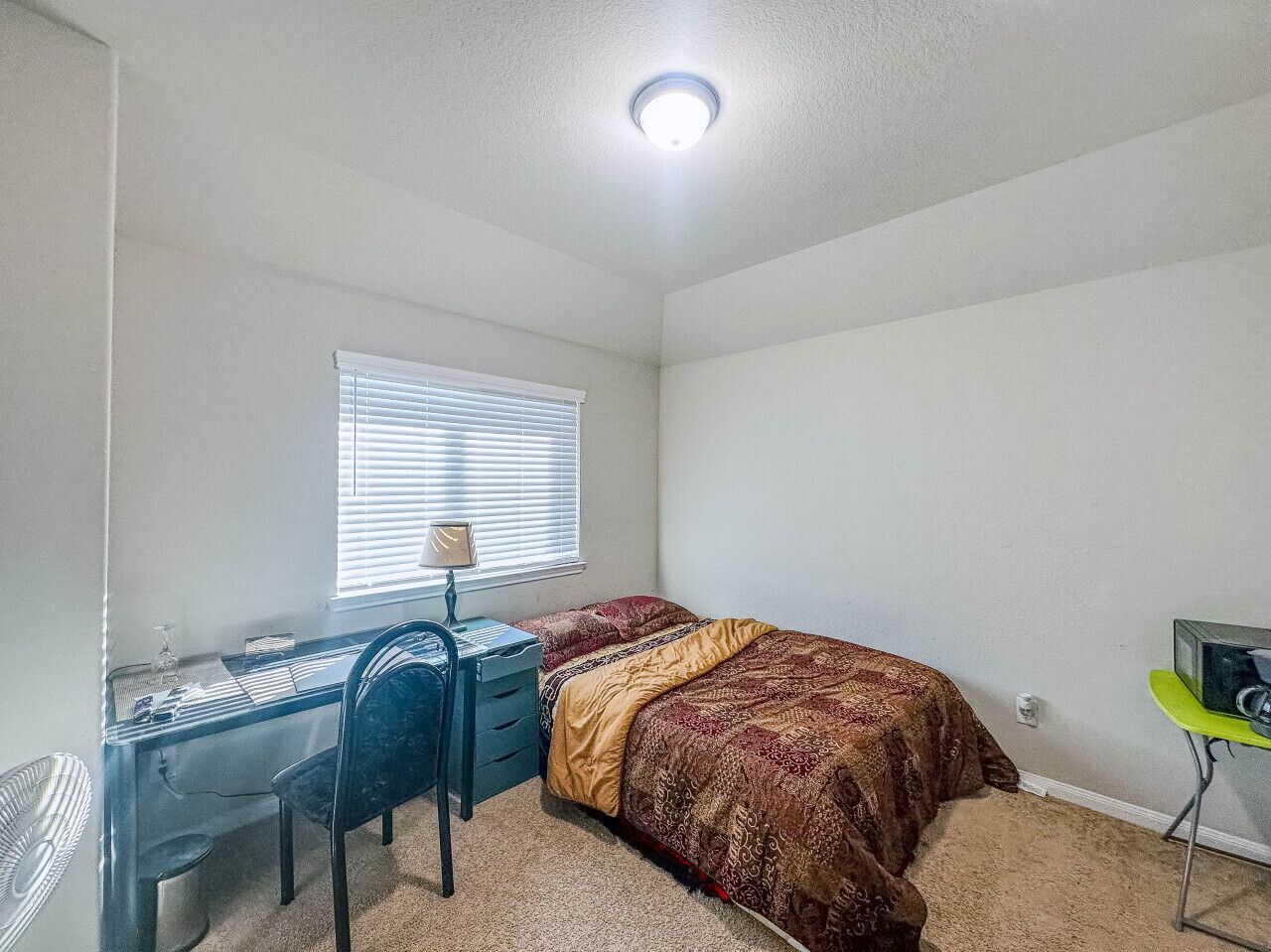 A bedroom with a bed, a desk, and a chair.