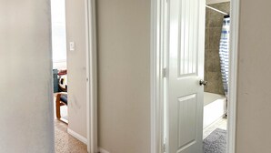 A hallway with a white door leading to a bathroom with a bathtub and a striped shower curtain. - Alpha Group - Room 2 (Richmond)