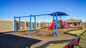A playground with swings, a red slide, and a blue climbing structure. - Alpha Group - Room 2 (Richmond)