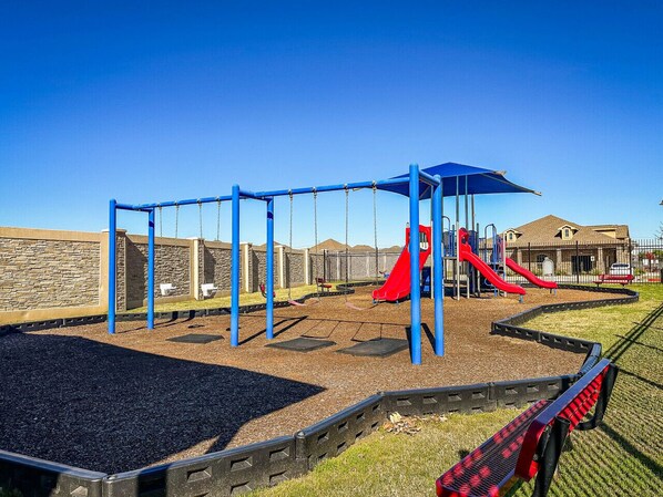 Un parque infantil con columpios, un tobogán rojo y una estructura azul para escalar.