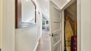 Un couloir avec un plancher en bois, un miroir et une porte qui donne sur une pièce où se trouve une valise.
