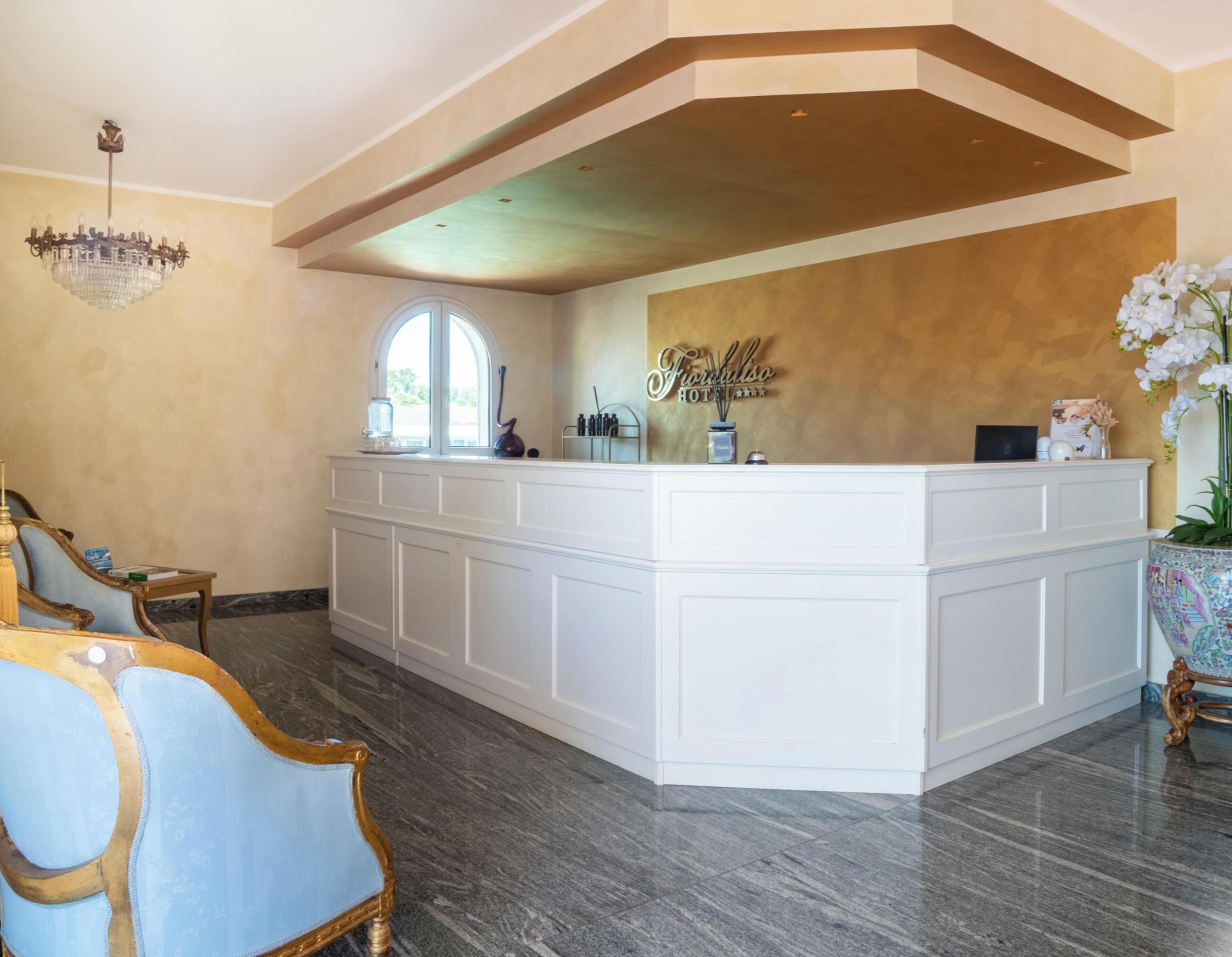 Un comptoir d’accueil orné d’un lustre, une grande fenêtre et une enseigne indiquant « Hôtel Forulso ».