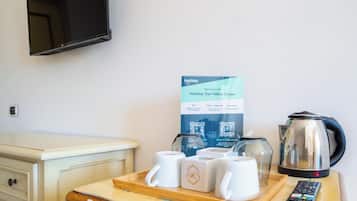 A hotel room with a wooden tray holding white mugs, a kettle, and a remote control on a wooden table.