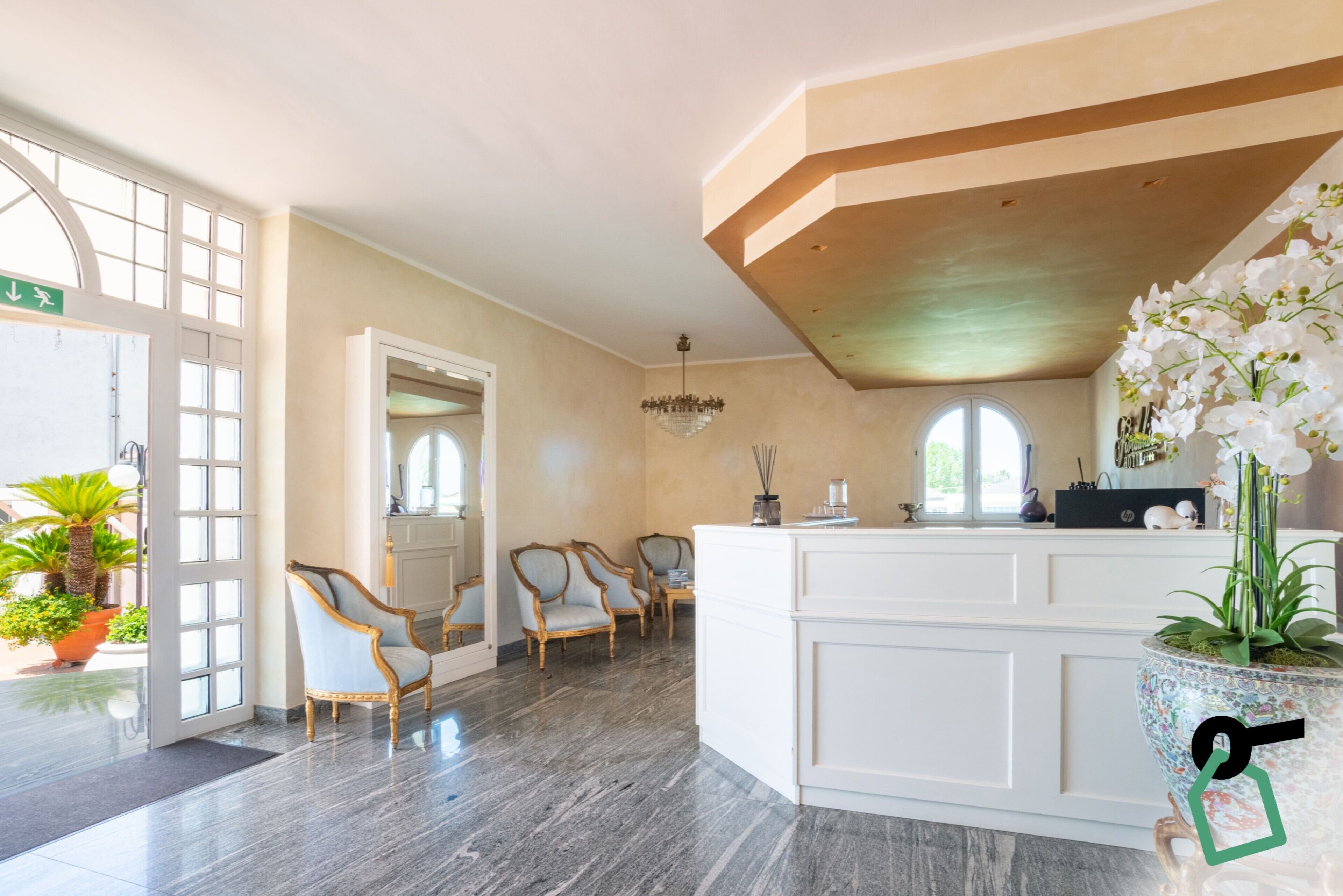 Un área de recepción con piso de mármol, sillas de madera, una mesa de recepción y un ventanal grande.