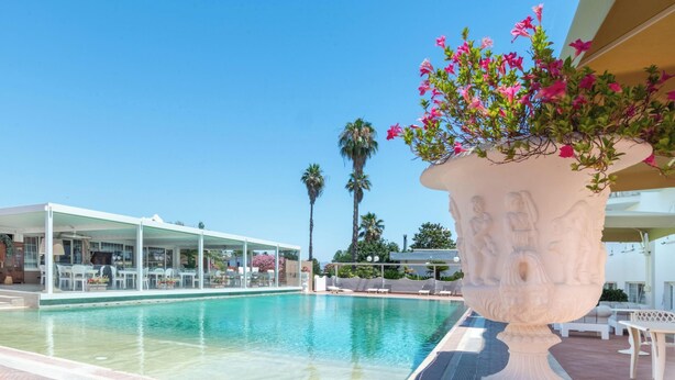 Une piscine à l’eau claire, un espace détente abrité et un grand bac à fleurs décoratif orné de fleurs roses.