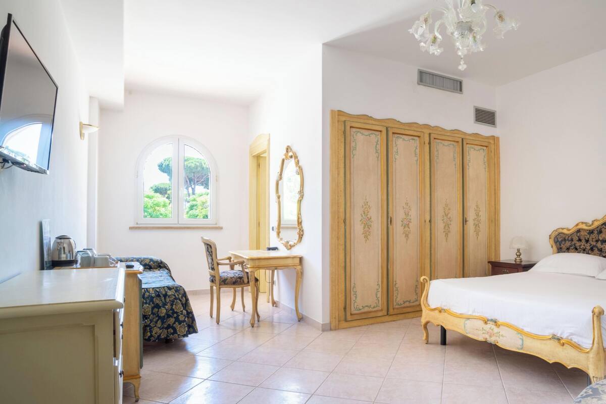 Una camera da letto con un letto, una scrivania, una sedia, un armadio e una finestra vista verde.