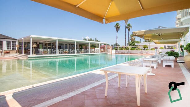 A pool area with a covered seating area, a pool, and a building with a balcony. - Hotiday San Felice Circeo (San Felice Circeo)