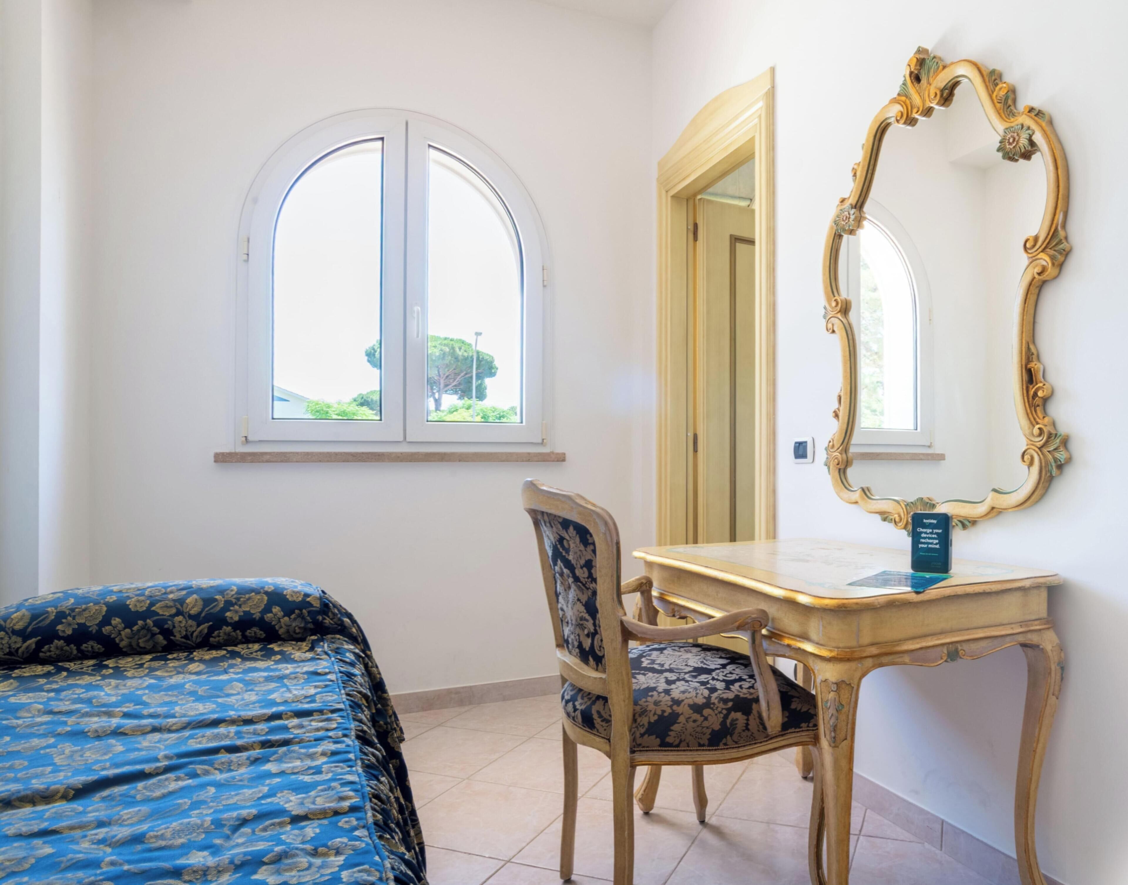 Una habitación con una cama, un escritorio, una silla, un espejo grande y una ventana.