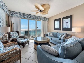 A spacious living room with a balcony overlooking the ocean, furnished with wicker chairs and a blue sofa. - Gulf Front 3/3 Summerwind 9th floor. Sunny and Chair (Navarre Beach)
