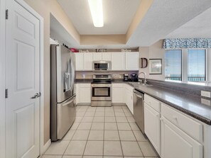 A modern kitchen with white cabinets, stainless steel appliances, and a tiled floor. - Gulf Front 3/3 Summerwind 9th floor. Sunny and Chair (Navarre Beach)