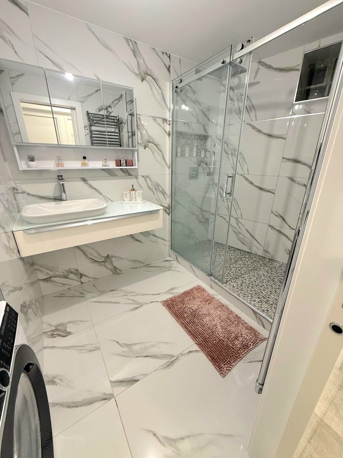 Une salle de bain moderne avec un sol en marbre, une douche à parois de verre et un meuble-lavabo doté d’un miroir et d’étagères.
