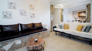 Ein Wohnzimmer mit einer Steinwand, einem schwarzen Ledersofa, einem weißen, flauschigen Sofa und einem Holztisch.